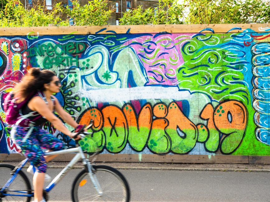 Cyclist passing COVID-19 graffitti in Dundee, Scotland.  DD065