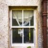 Curtained window of an abandoned croft house, near Callakille, Scotland.